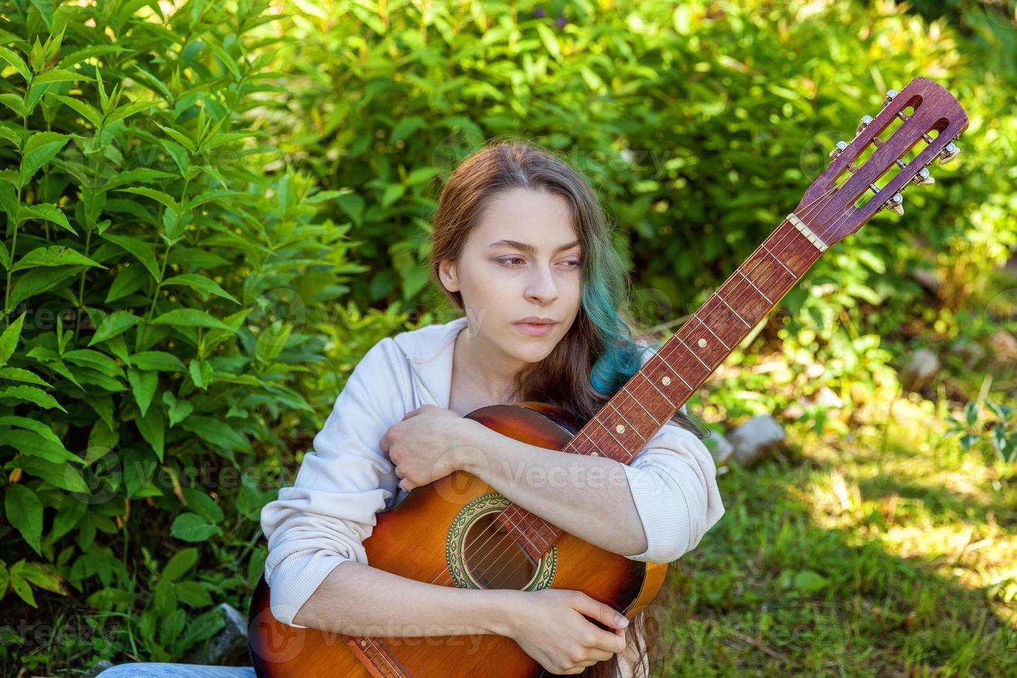 joven mujer sentado en césped y jugando guitarra foto