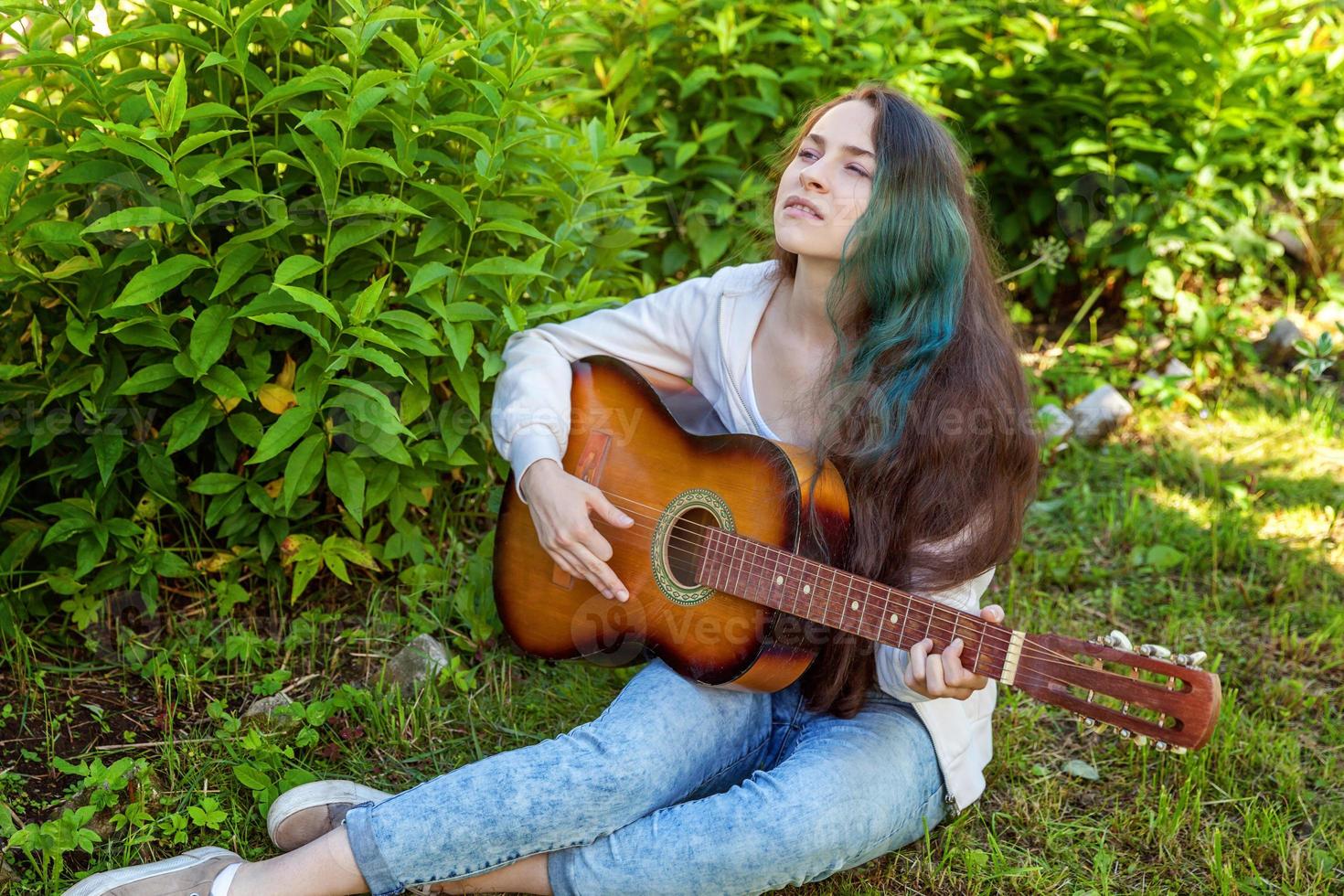 joven mujer sentado en césped y jugando guitarra foto