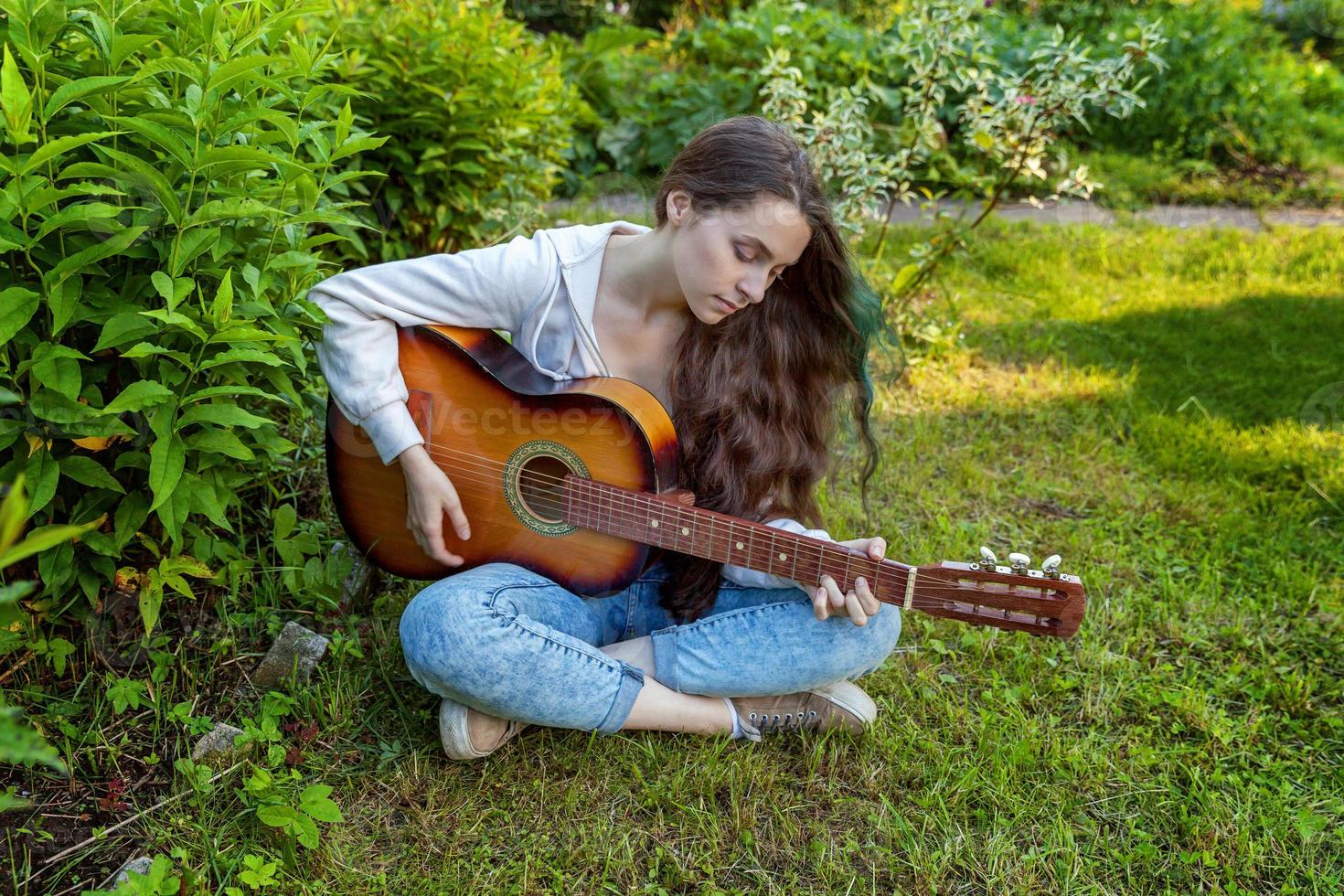 Young woman sitting in grass and playing guitar photo