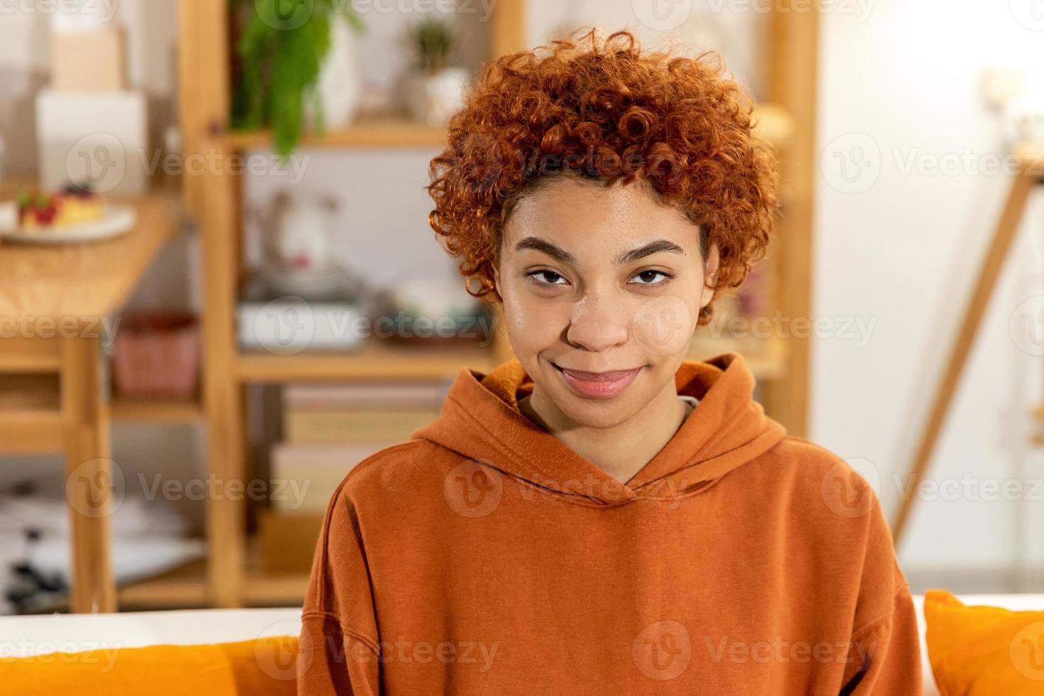 Beautiful african american girl with afro hairstyle smiling sitting on sofa at home indoor. Young african woman with curly hair smiling. Freedom happiness carefree happy people concept. photo