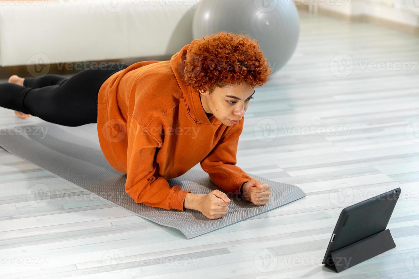 aptitud rutina de ejercicio capacitación. joven sano ajuste africano niña haciendo tablón ejercicio en yoga estera en piso a hogar. atlético mujer en ropa de deporte formación pilates deporte y aptitud física. foto