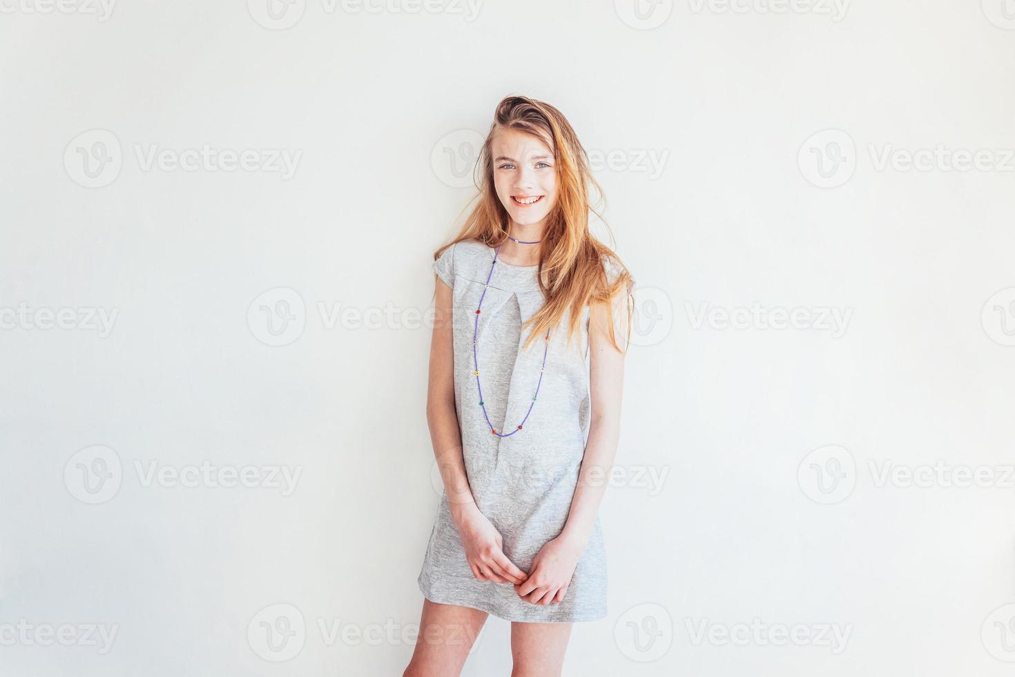 Happy teenage girl smiling. Closeup portrait young happy positive teen woman in grey dress against white wall background. European woman. Positive human emotion facial expression body language. photo