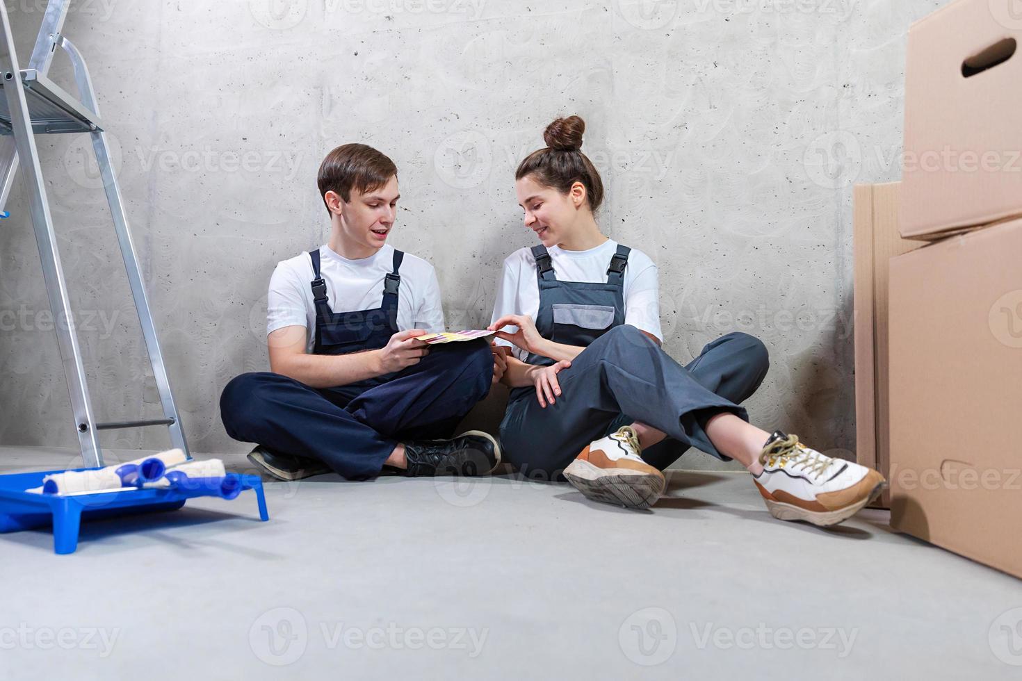 House decoration DIY renovation concept Happy couple sitting on floor in empty room of new home planning design. Husband and wife holding swatch palette choosing colors for painting wall in new house photo