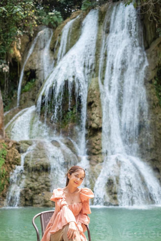 Young Asian woman sitting on a chair In front of the Khoun Moung Keo Waterfall photo