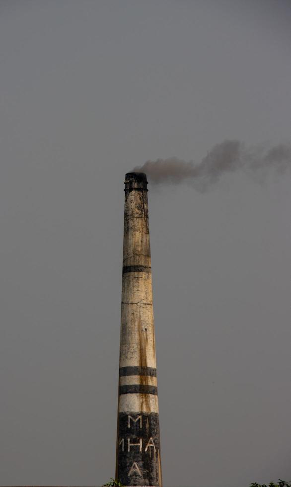 Industrial brick kiln close-up view with dark smoke coming out from the chimney. The pipe of an industrial brick kiln plant with a dark ash background. Environmental pollution with a dark brick kiln. photo