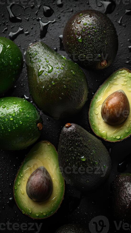 Top view Fresh avocados on black background. Organic avocado with seed, avocado halves and whole fruits on black background. Top view. Pop art design, creative summer food concept. photo