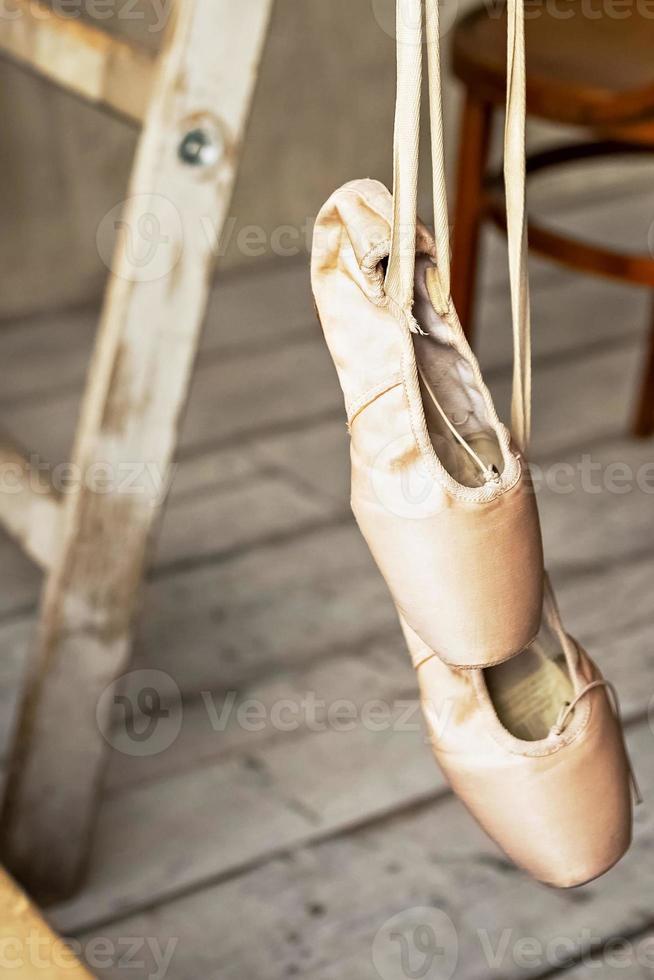 Ballet shoes hang on a crossbar in the dance hall. Dance concept, ballet school, shoes for ballerinas. New pointe shoes with satin ribbons hanging on them. photo