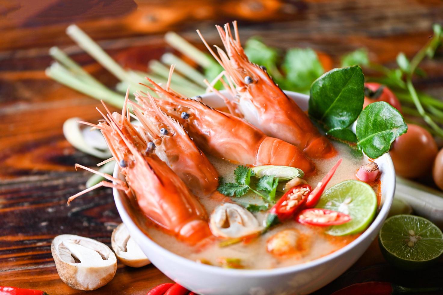 Thai Food Tom Yum Kung, Hot and sour spicy shrimps prawns soup  curry lemon lime galangal red chili straw mushroom on table food, Shrimp soup on seafood soup bowl with thai herb and spices photo