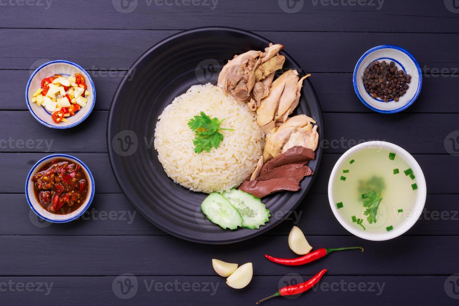 Hainanese chicken rice on a black wooden table background steamed chicken rice with chicken soup, sauces condiments Asian food Thailand China Singapore, top view photo