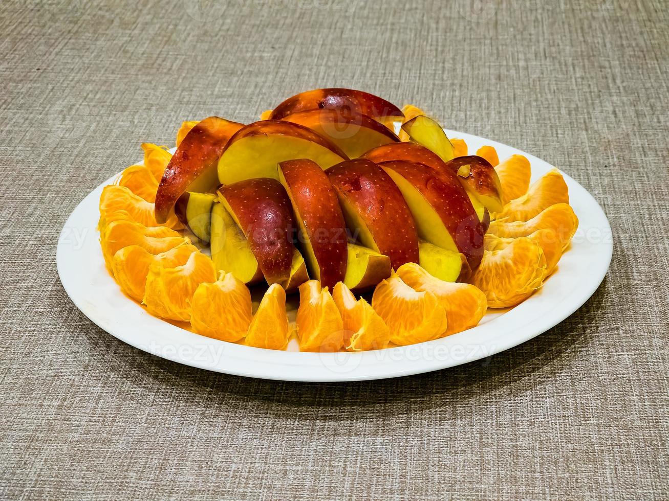 Peeled tangerines sliced and red and yellow apples cut into slices on a white plate. Healthy food concept. photo