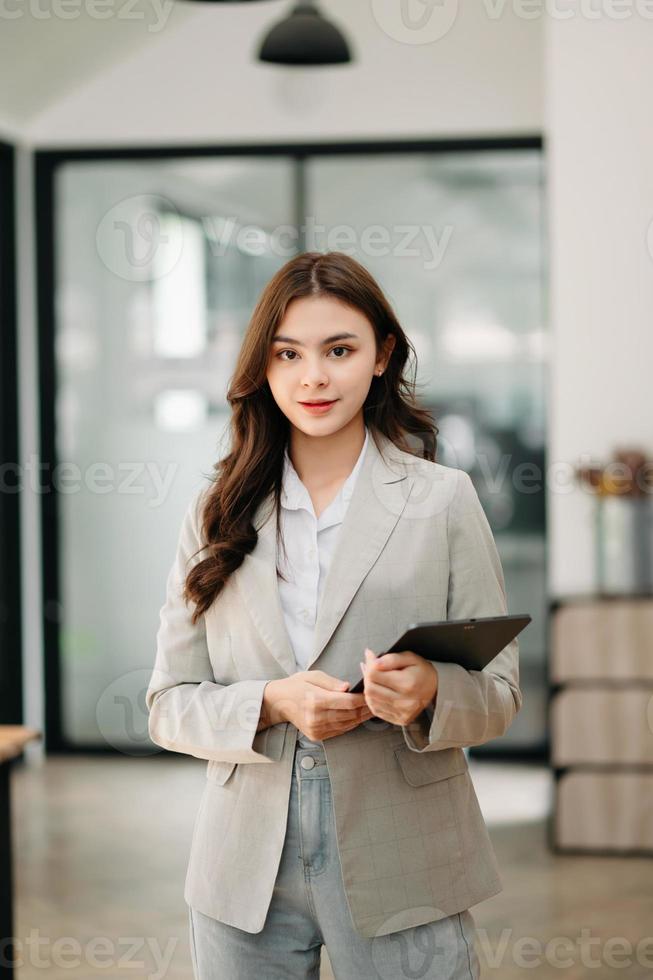 Confident business expert attractive smiling young woman holding digital tablet  on desk in creative office. photo