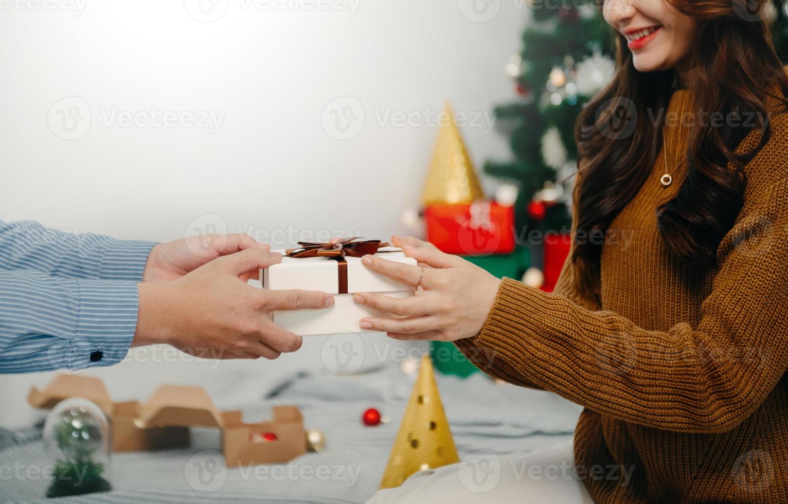 Christmas Gift in hands. Happy Man giving Christmas and New Year Gift box to woman at Home. Family Xmas celebration. Christmas decoration. photo