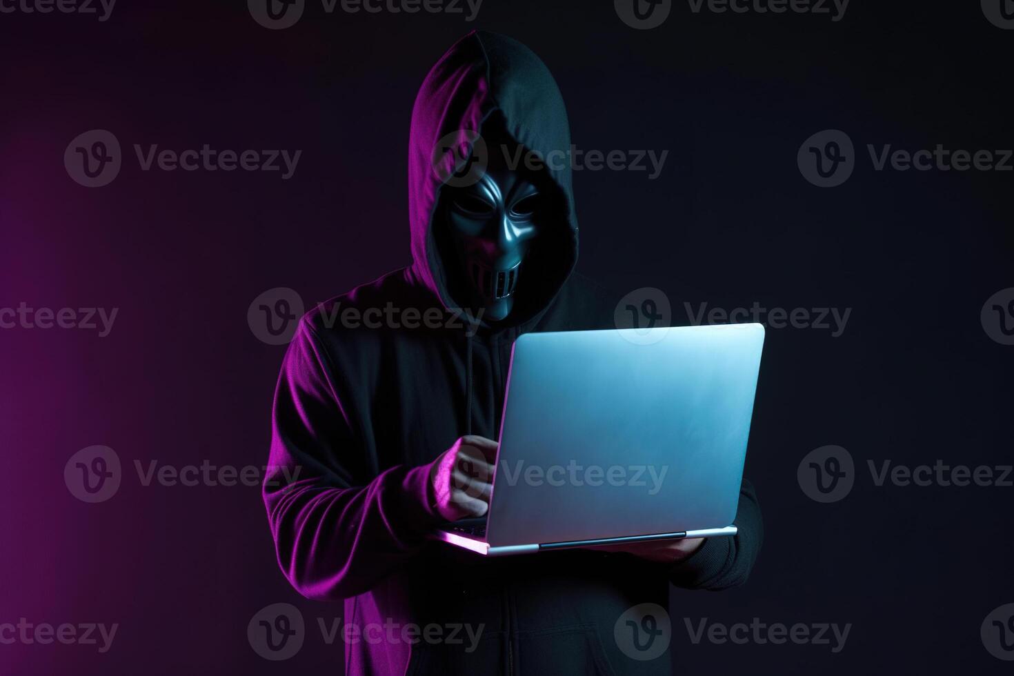 a hacker in a hoodie using a laptop computer isolated on dark background with neon light. photo