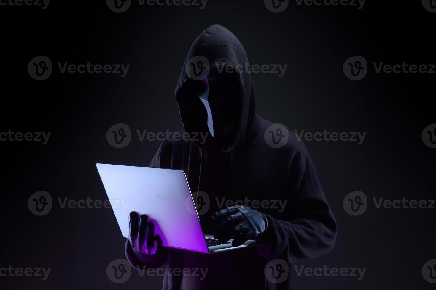 a hacker in a hoodie using a laptop computer isolated on dark background with neon light. photo