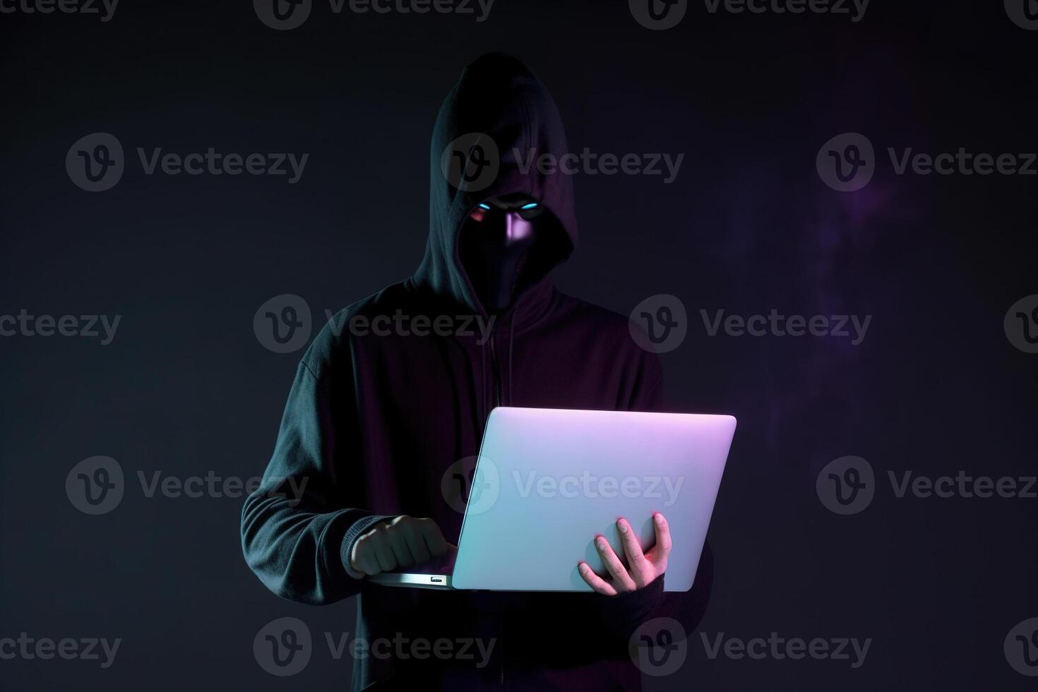 a hacker in a hoodie using a laptop computer isolated on dark background with neon light. photo
