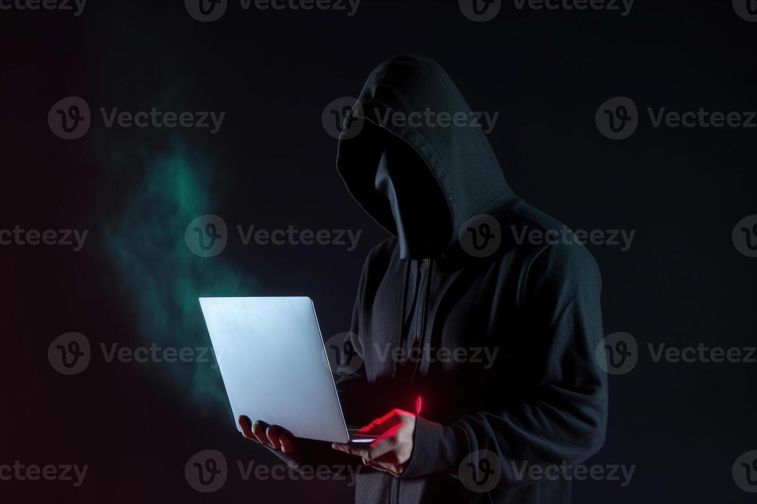 a hacker in a hoodie using a laptop computer isolated on dark background with neon light. photo