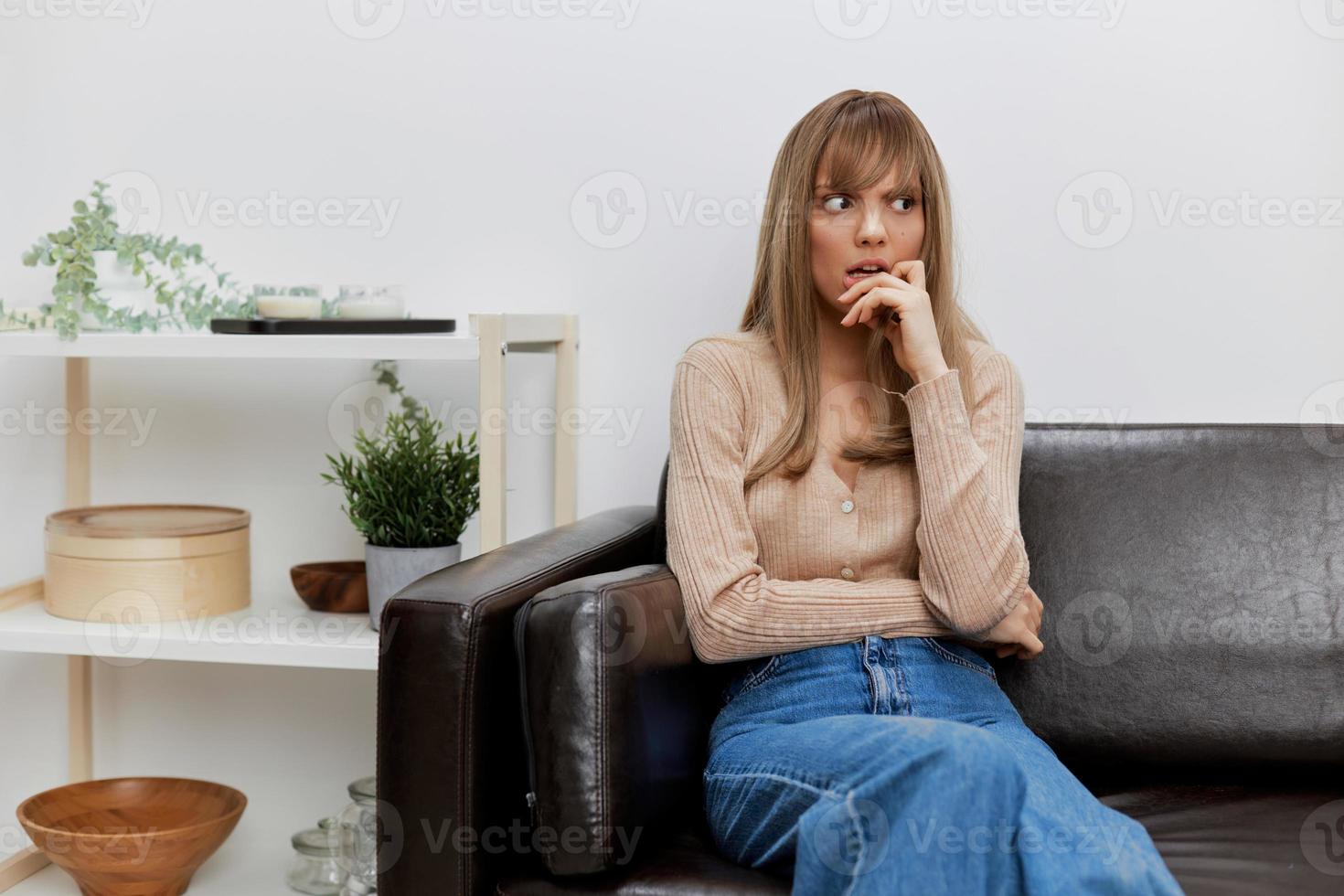 Thoughtful pensive blonde lady in casual sweater reflects on future plans looks aside sitting in sofa at modern interior. Female client have shrink appointment in psychological help office. Copy space photo