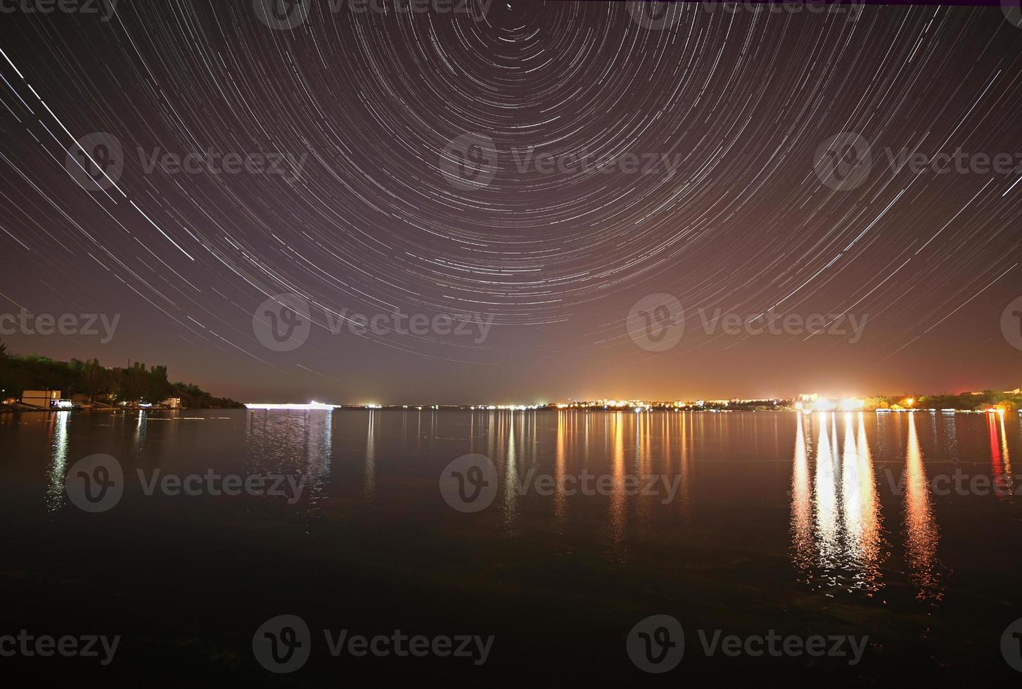 tracks of stars in night sky above river photo