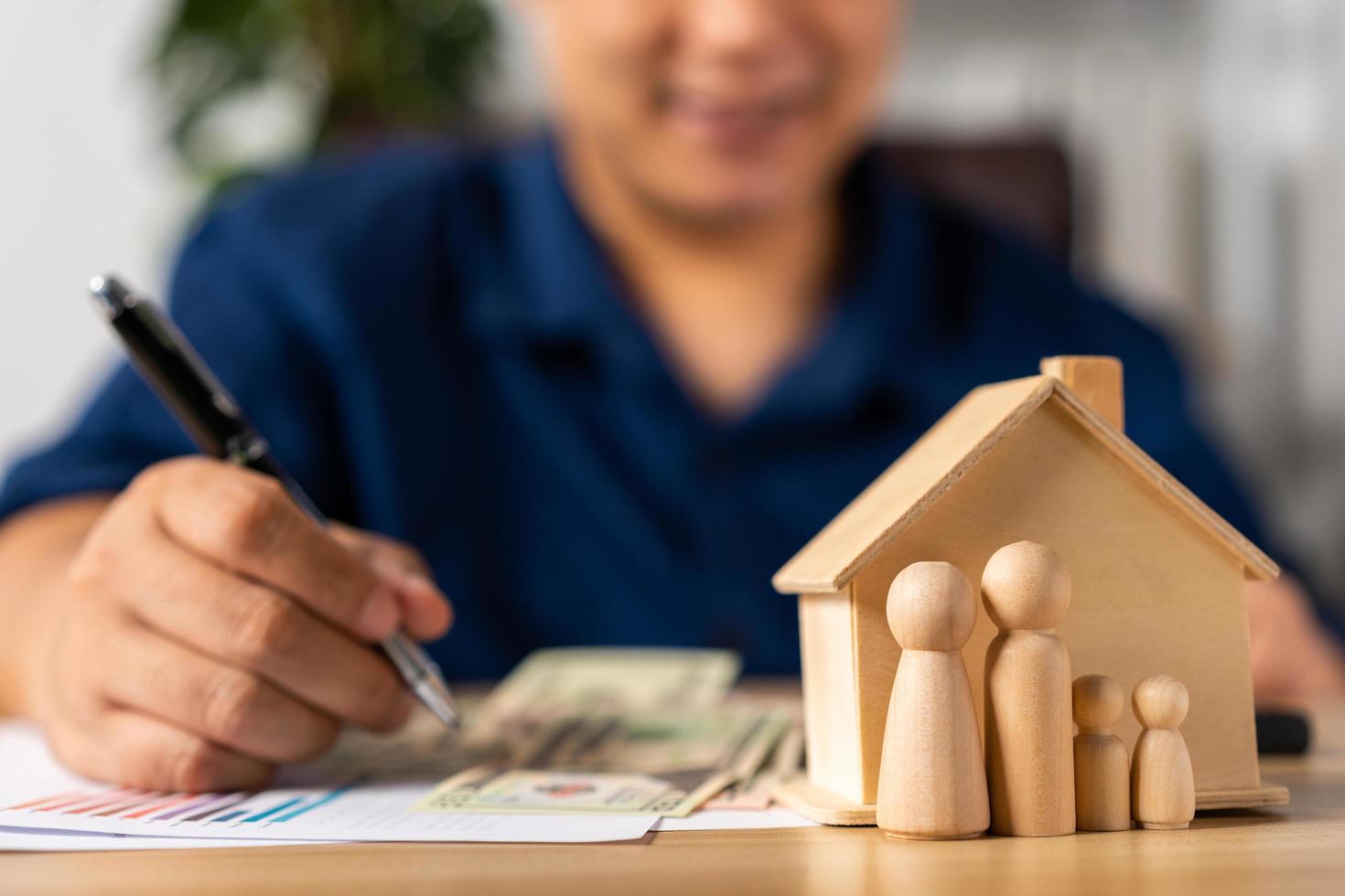 Selective focus for House model and figures people in front Happy Asian man holding a banknote and do financial accounting, Concept for financial planning, mortgage estate, Insurance, and home loan photo