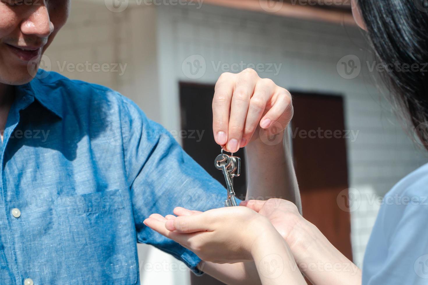 Happy smiling couple in front of the home and holding keys to New Home On Moving In Day, and start a new life family. Concept of homeowner and relocation photo