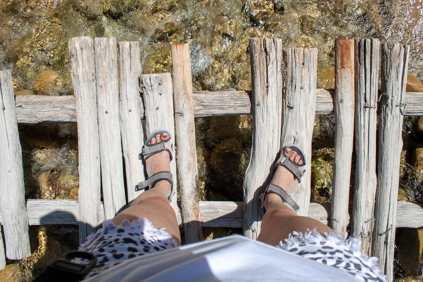 Woman's legs on an old wooden bridge through the river photo
