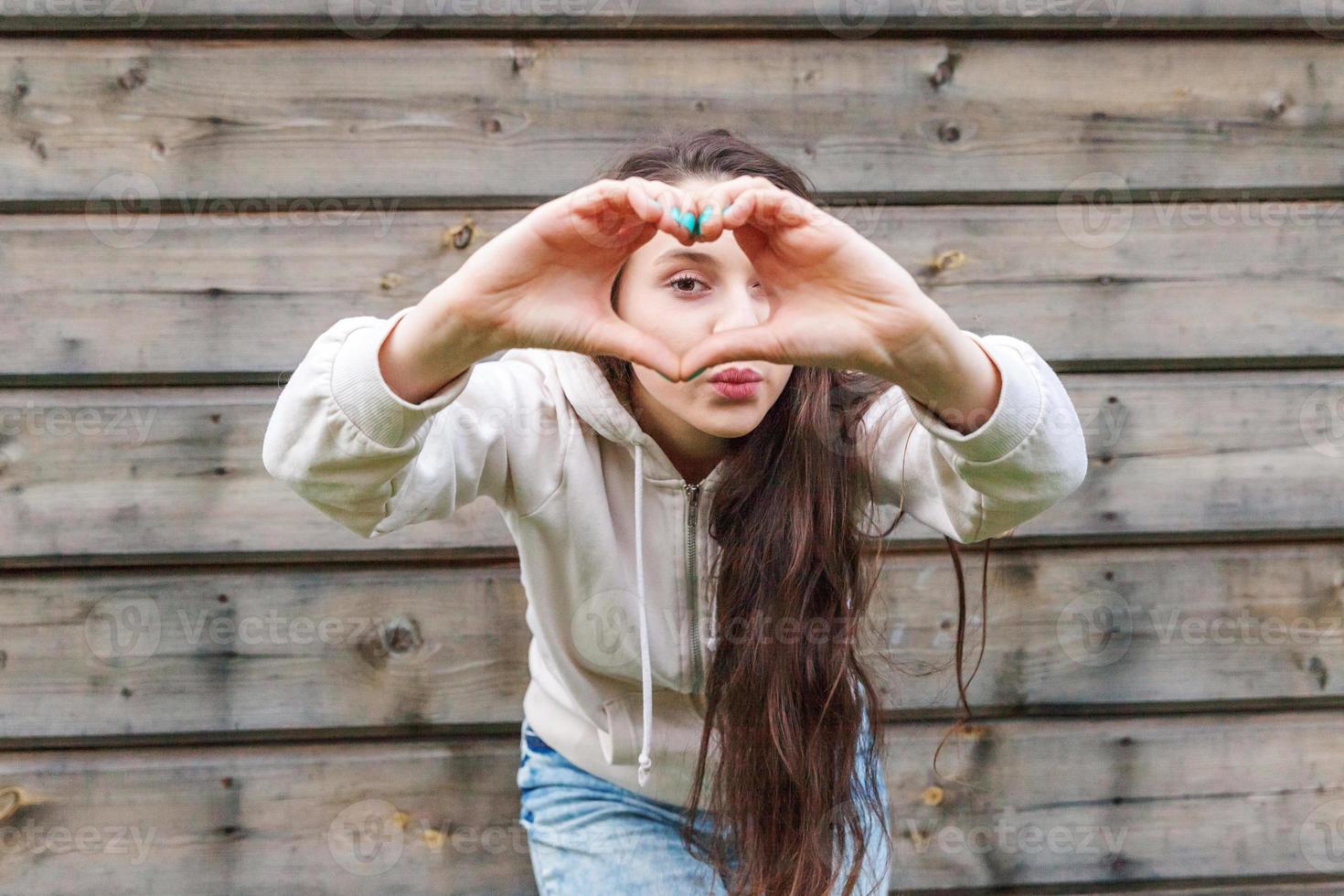 Love, heart shape, peace. Beauty portrait young happy positive woman showing heart sign with hands on wooden wall background photo