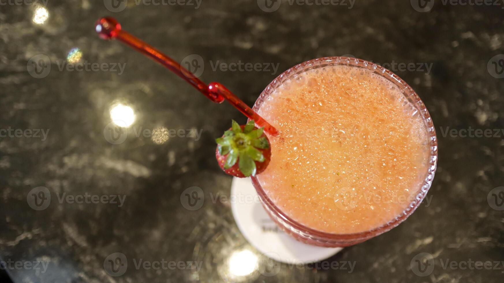 A glass of strawberry juice at the table with a fancy straw. photo