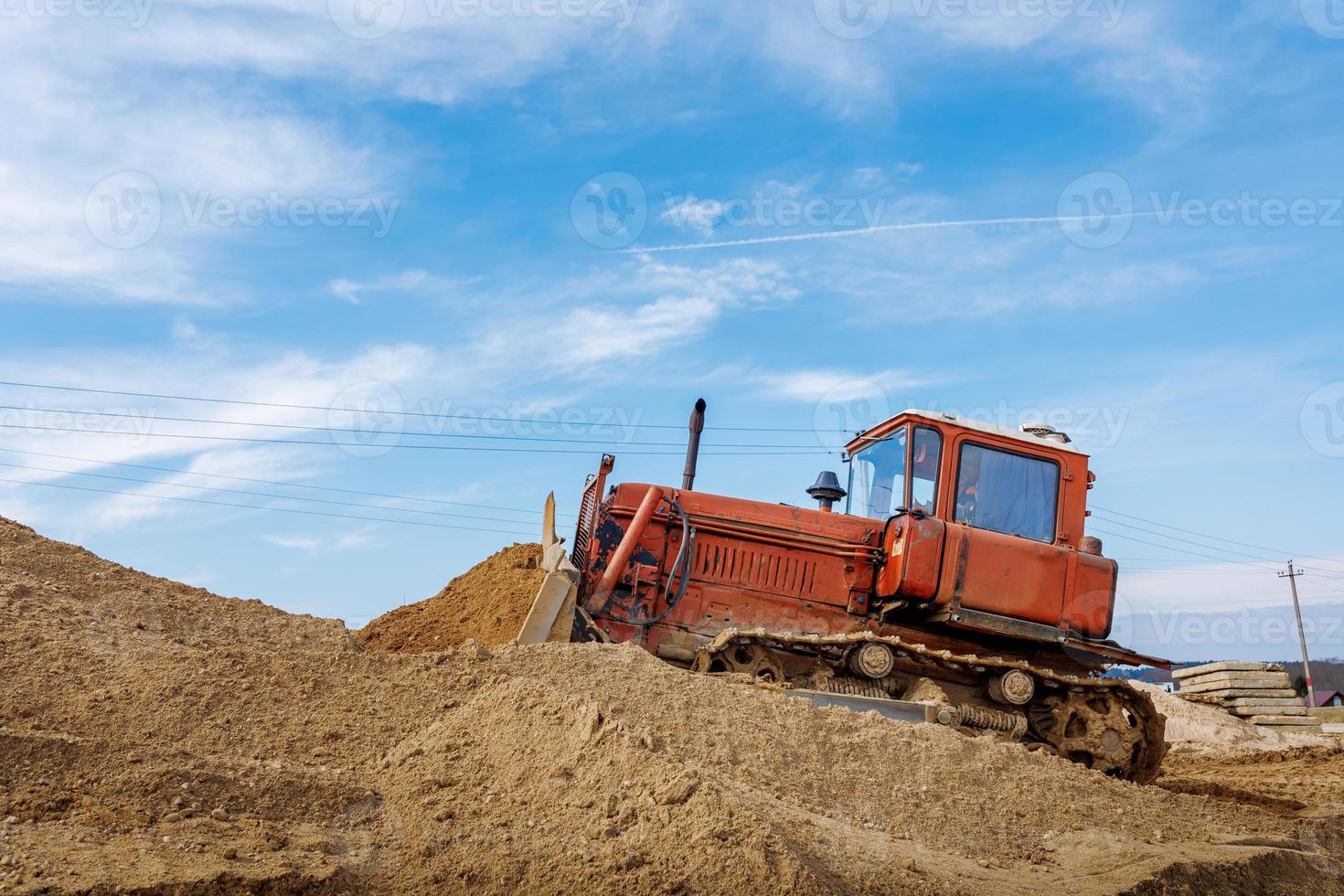 un antiguo naranja excavadora realiza trabajo a nivel el arenoso suelo foto