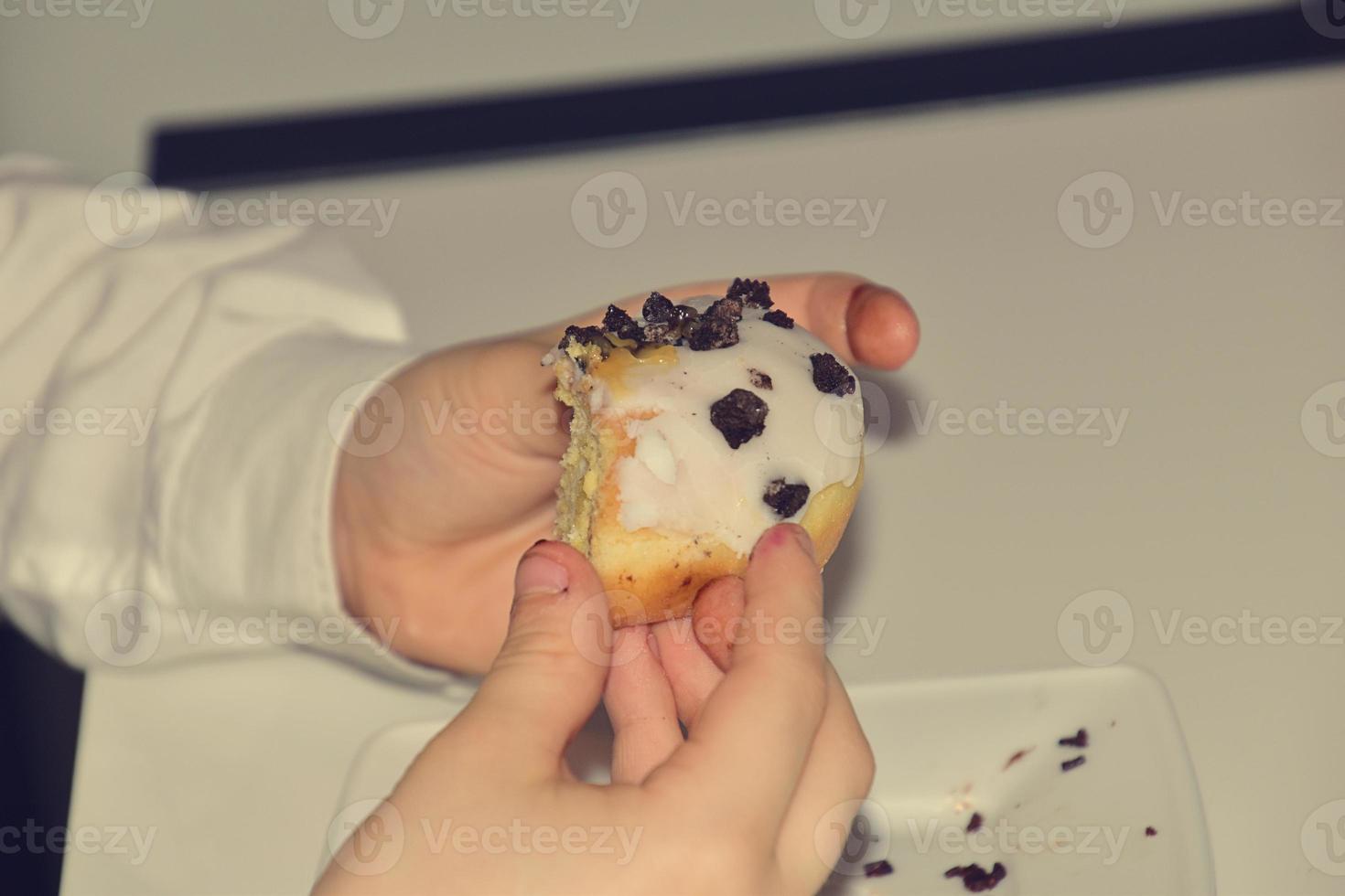 child's hand in a white shirt holding an icing-covered donut photo
