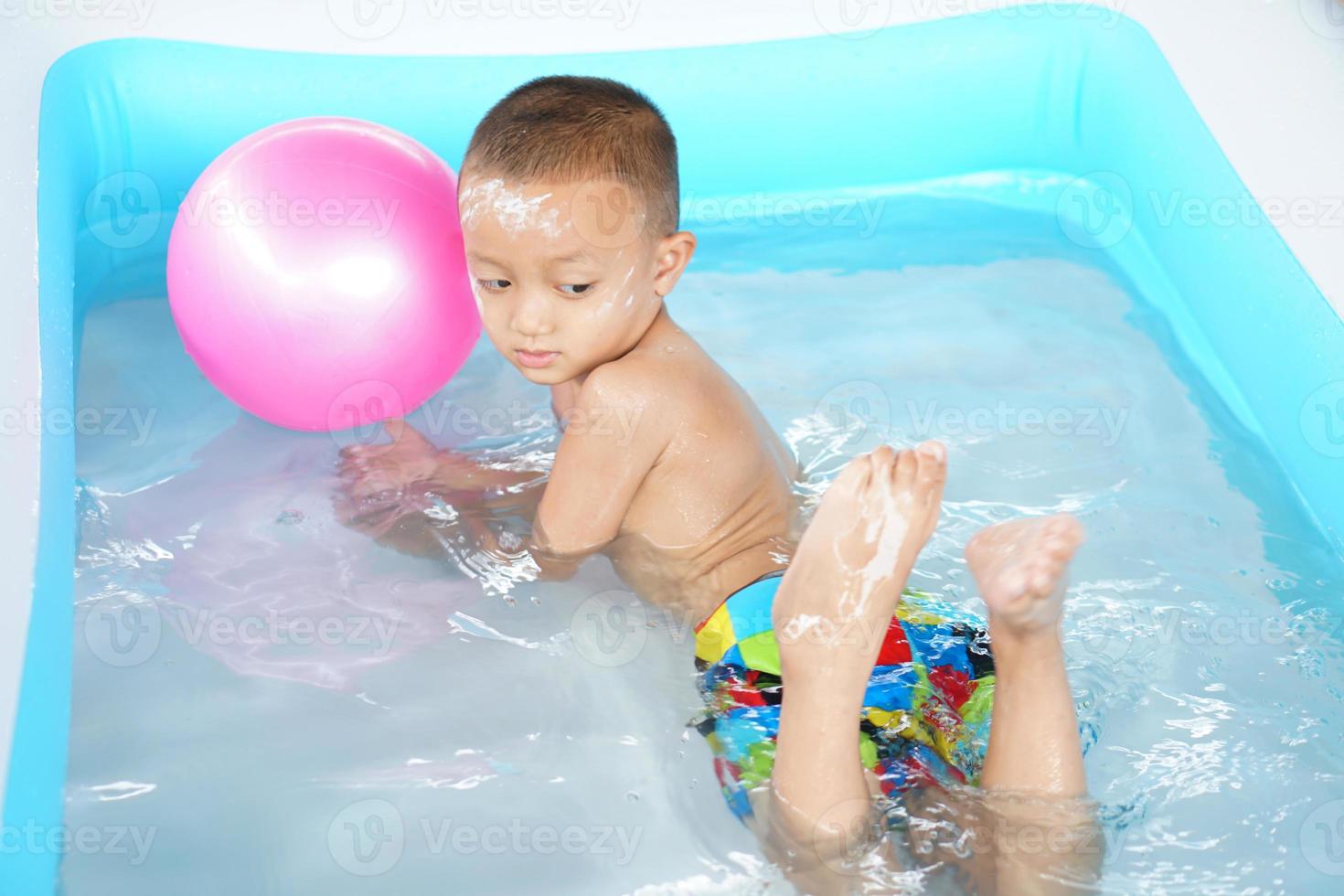 Hot weather. Boy playing with water happily in the tub. photo