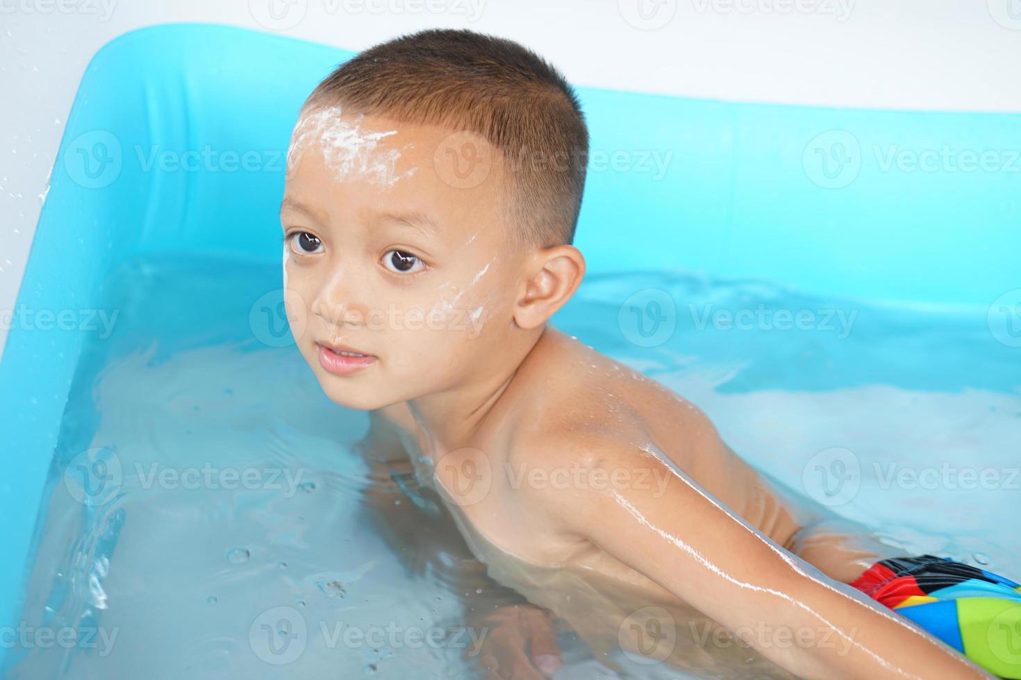 Hot weather. Boy playing with water happily in the tub. photo