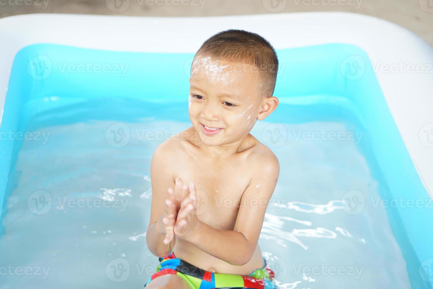 Hot weather. Boy playing with water happily in the tub. photo