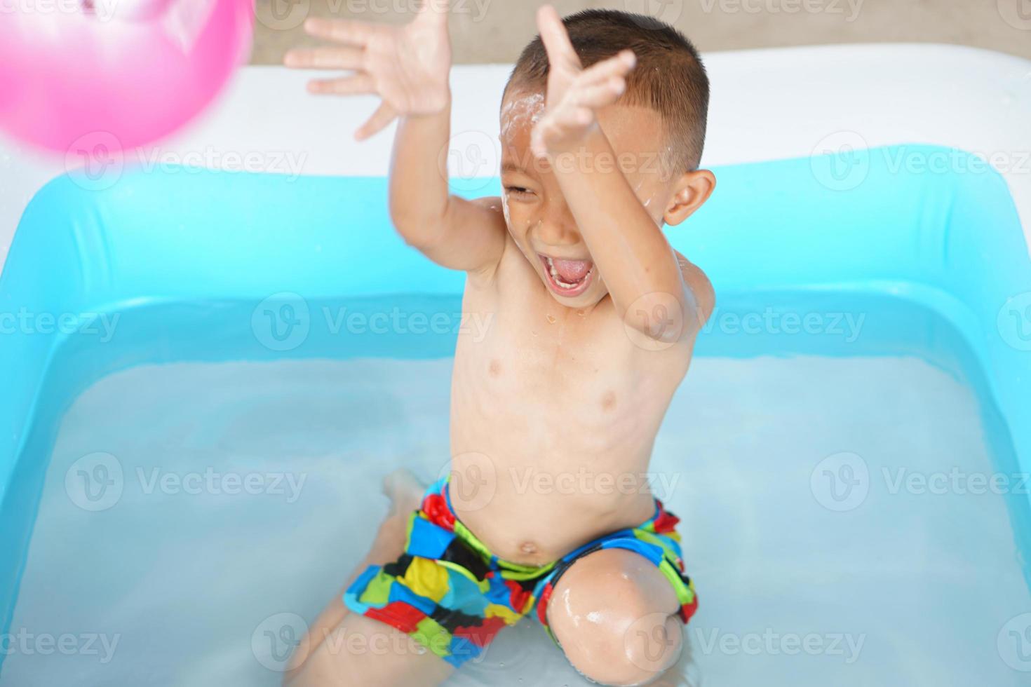 Hot weather. Boy playing with water happily in the tub. photo