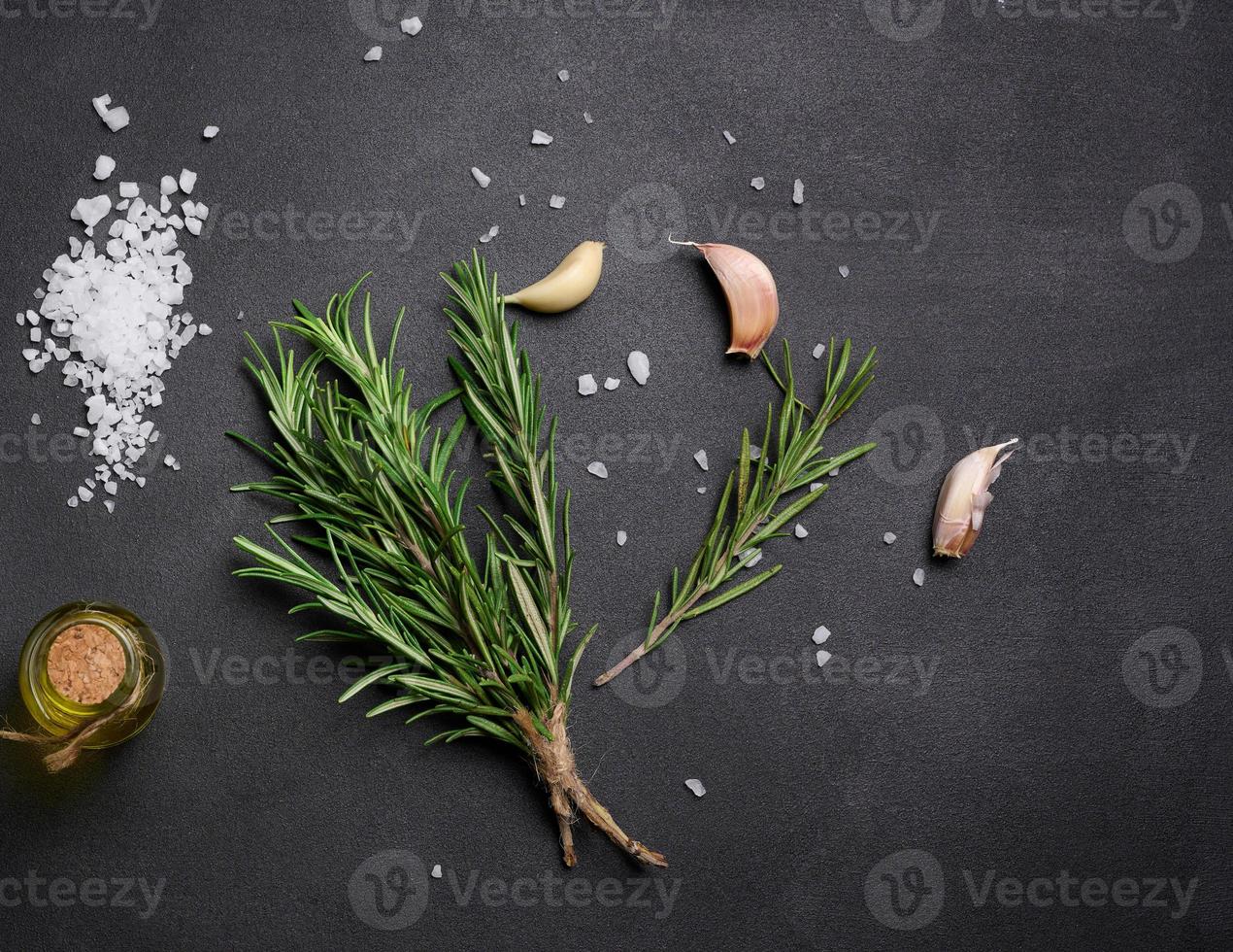 Scattered coarse white salt, peppercorns and rosemary sprigs on a black table, ingredients for cooking fish and meat photo