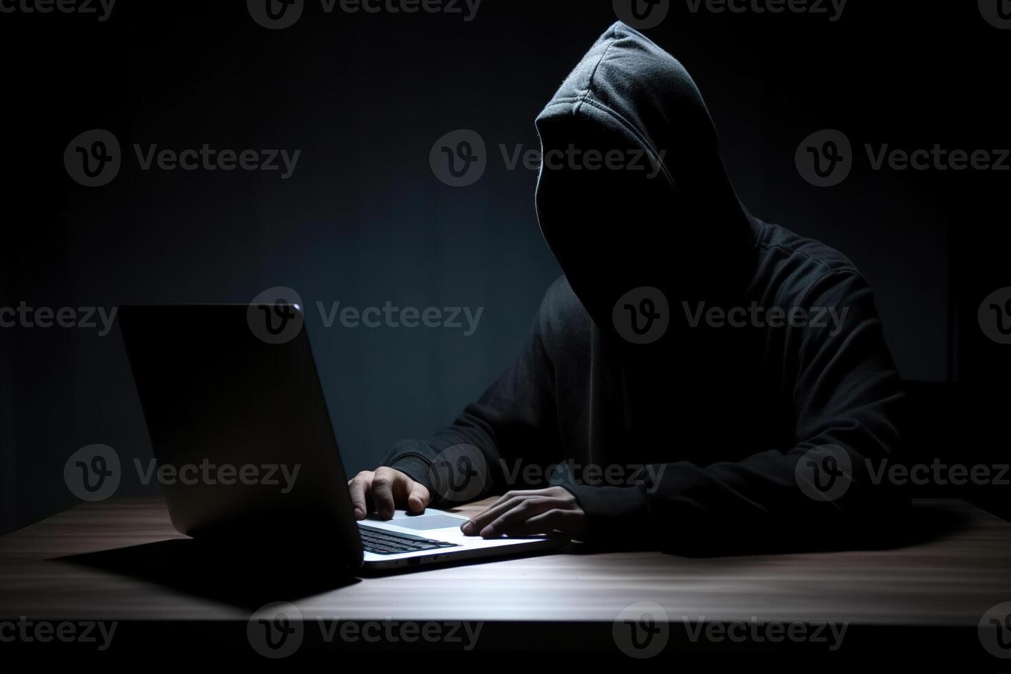 Hacker wearing black hoodie using laptop computer while working on dark background. photo