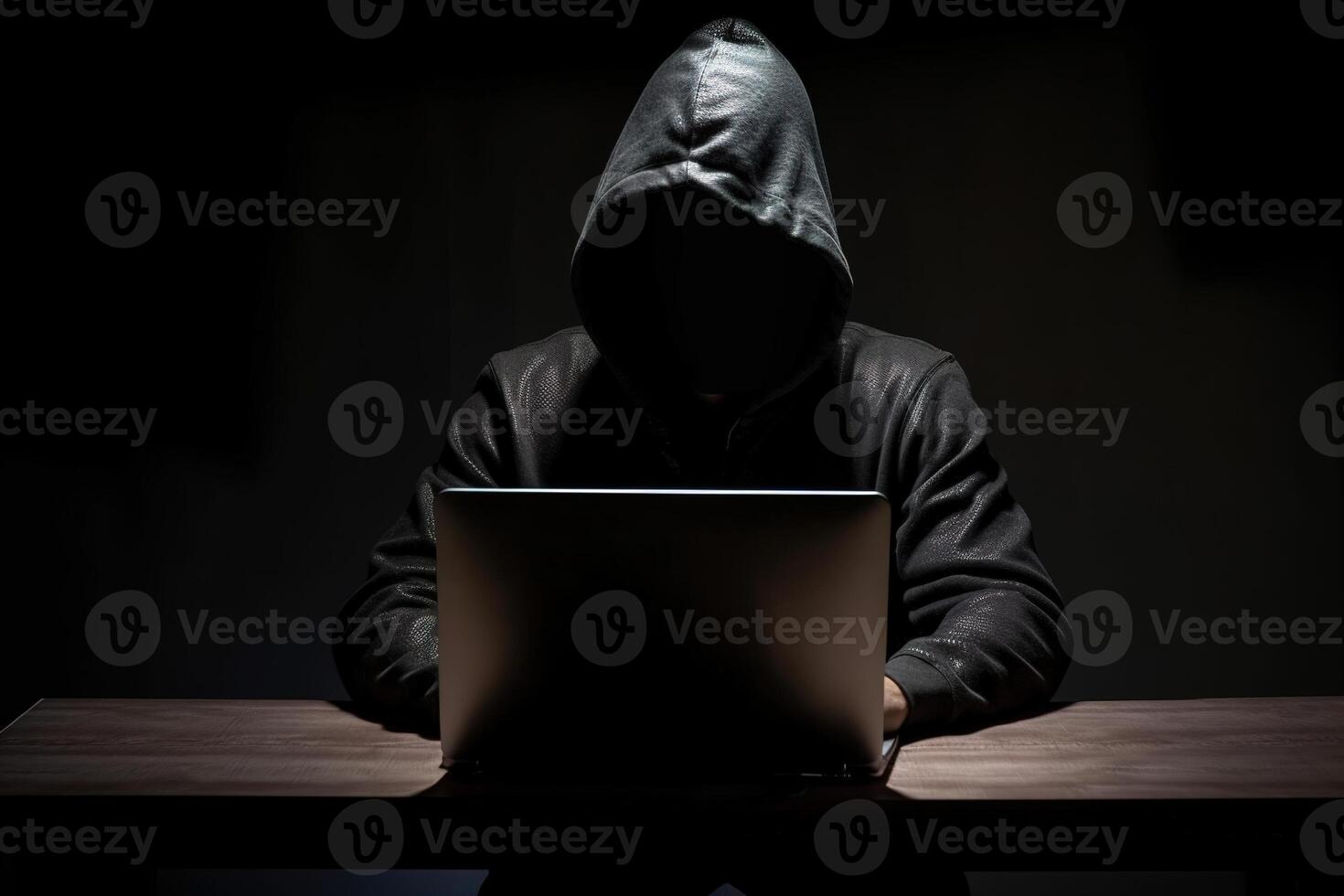 Hacker wearing black hoodie using laptop computer while working on dark background. photo