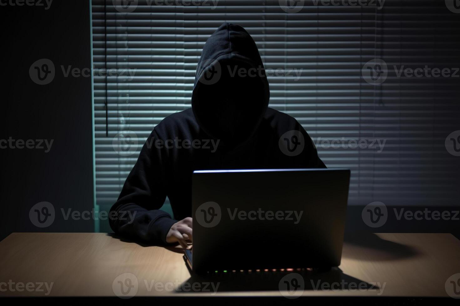 Hacker wearing black hoodie using laptop computer while working on dark background. photo