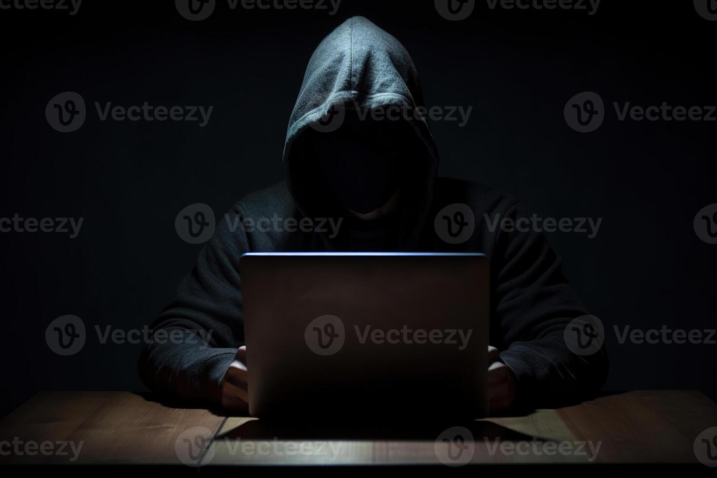 Hacker wearing black hoodie using laptop computer while working on dark background. photo