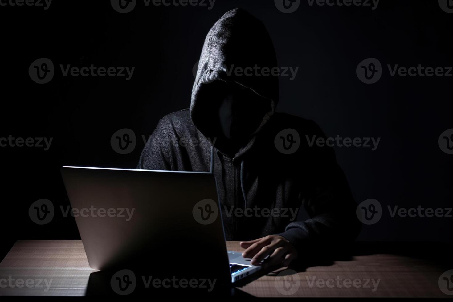 Hacker wearing black hoodie using laptop computer while working on dark background. photo