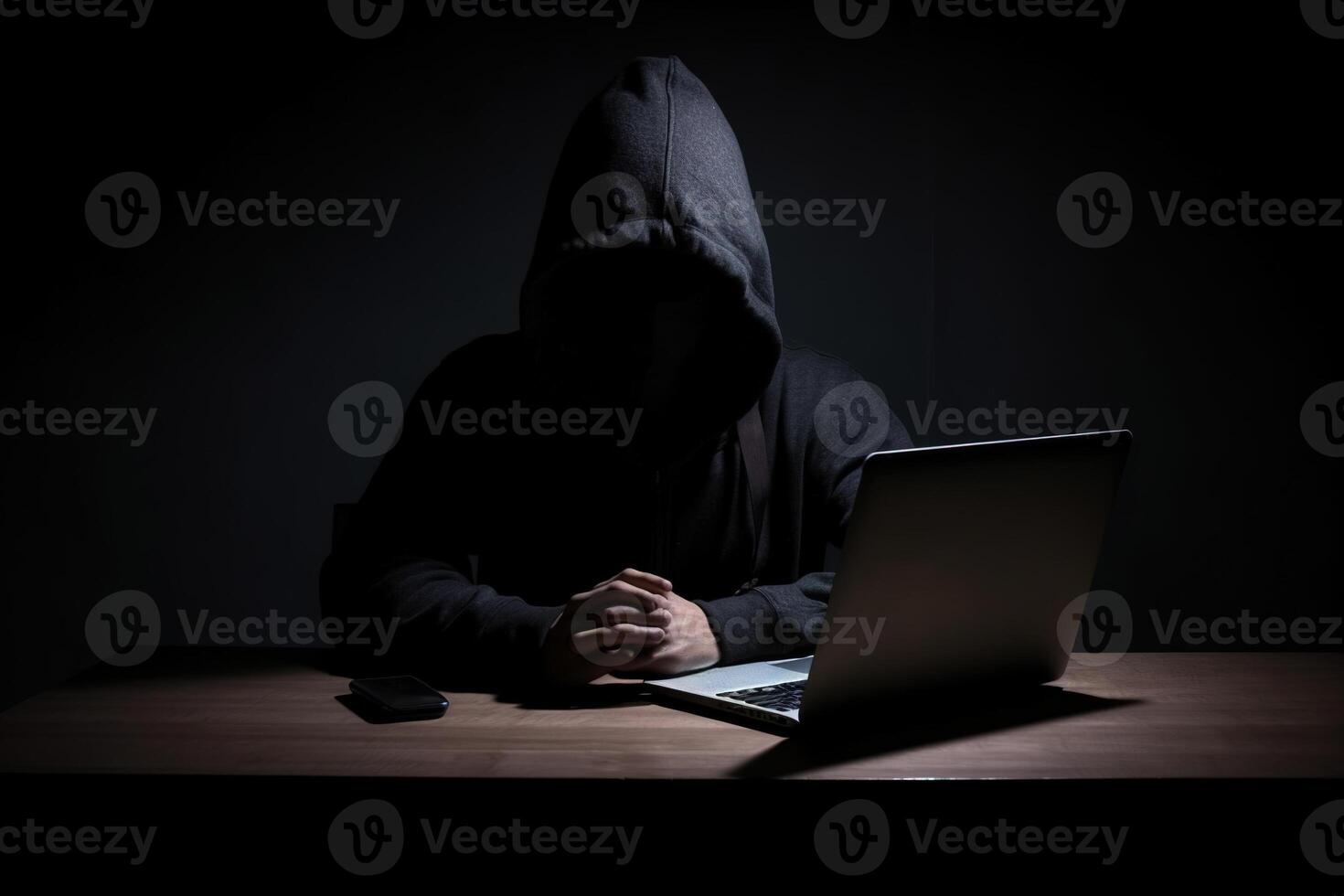 Hacker wearing black hoodie using laptop computer while working on dark background. photo