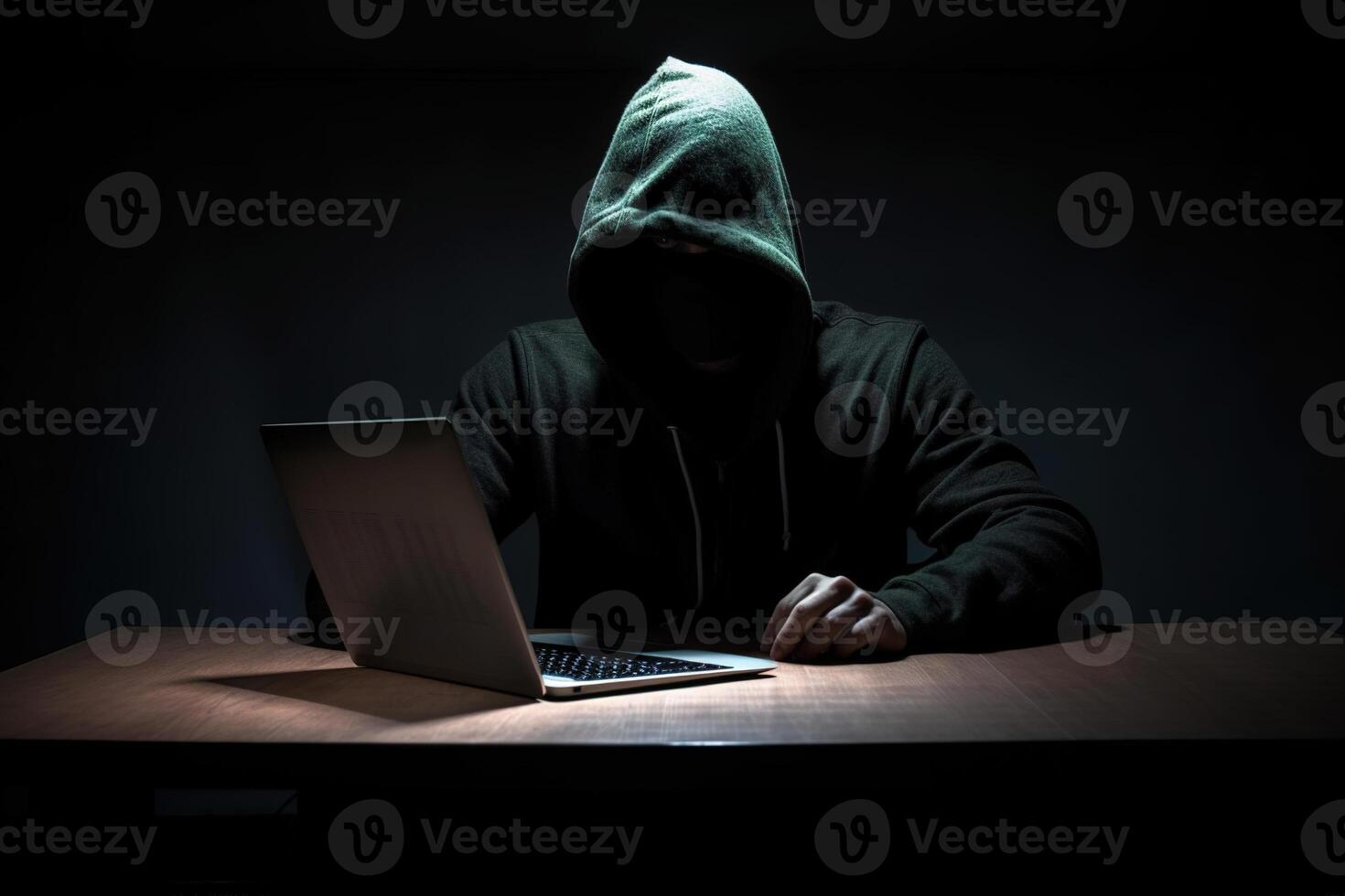 Hacker wearing black hoodie using laptop computer while working on dark background. photo