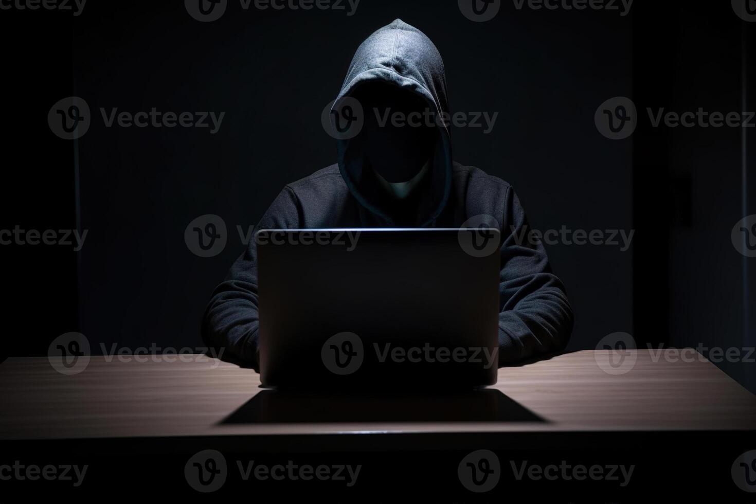 Hacker wearing black hoodie using laptop computer while working on dark background. photo