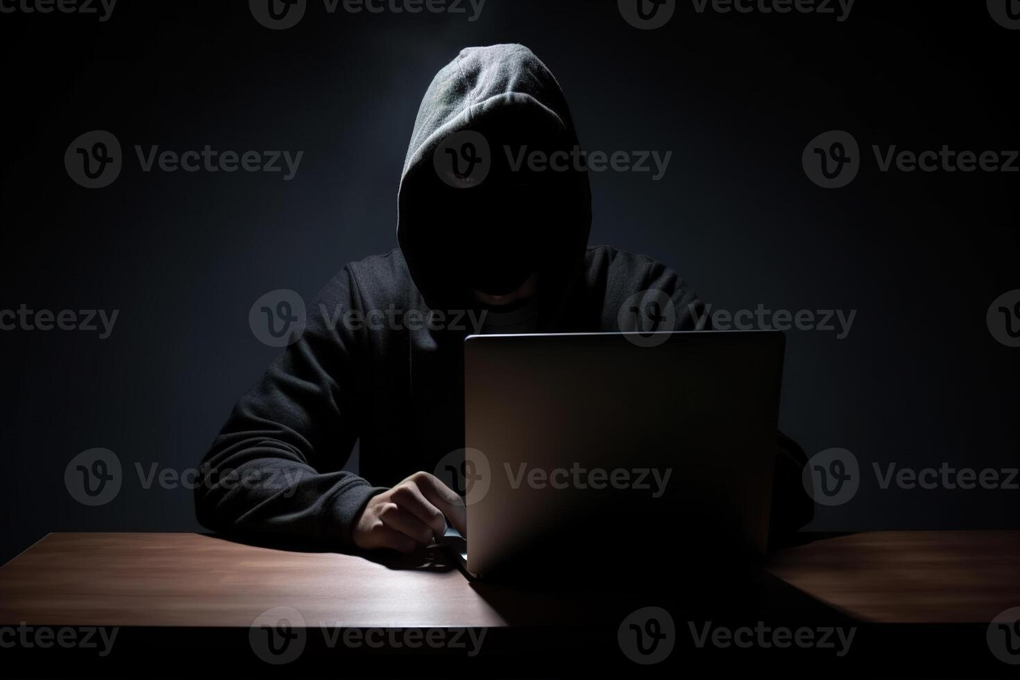 Hacker wearing black hoodie using laptop computer while working on dark background. photo