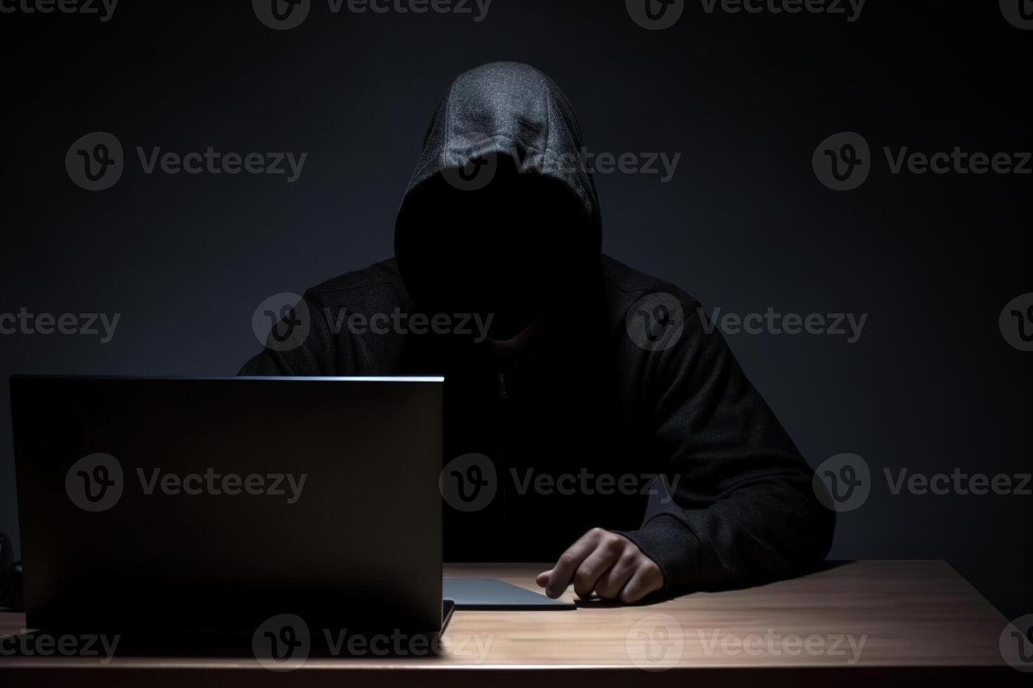 Hacker wearing black hoodie using laptop computer while working on dark background. photo