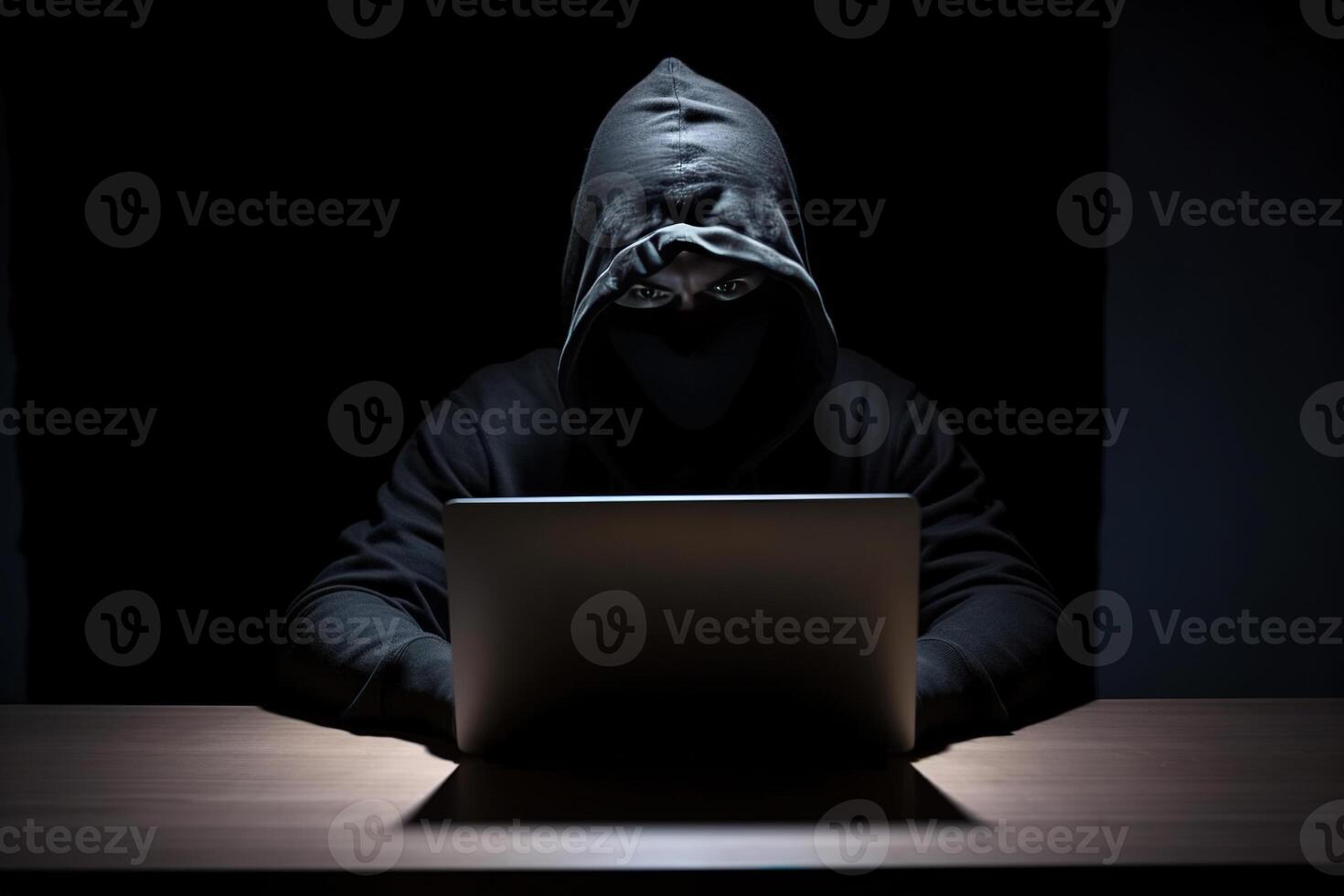 Hacker wearing black hoodie using laptop computer while working on dark background. photo