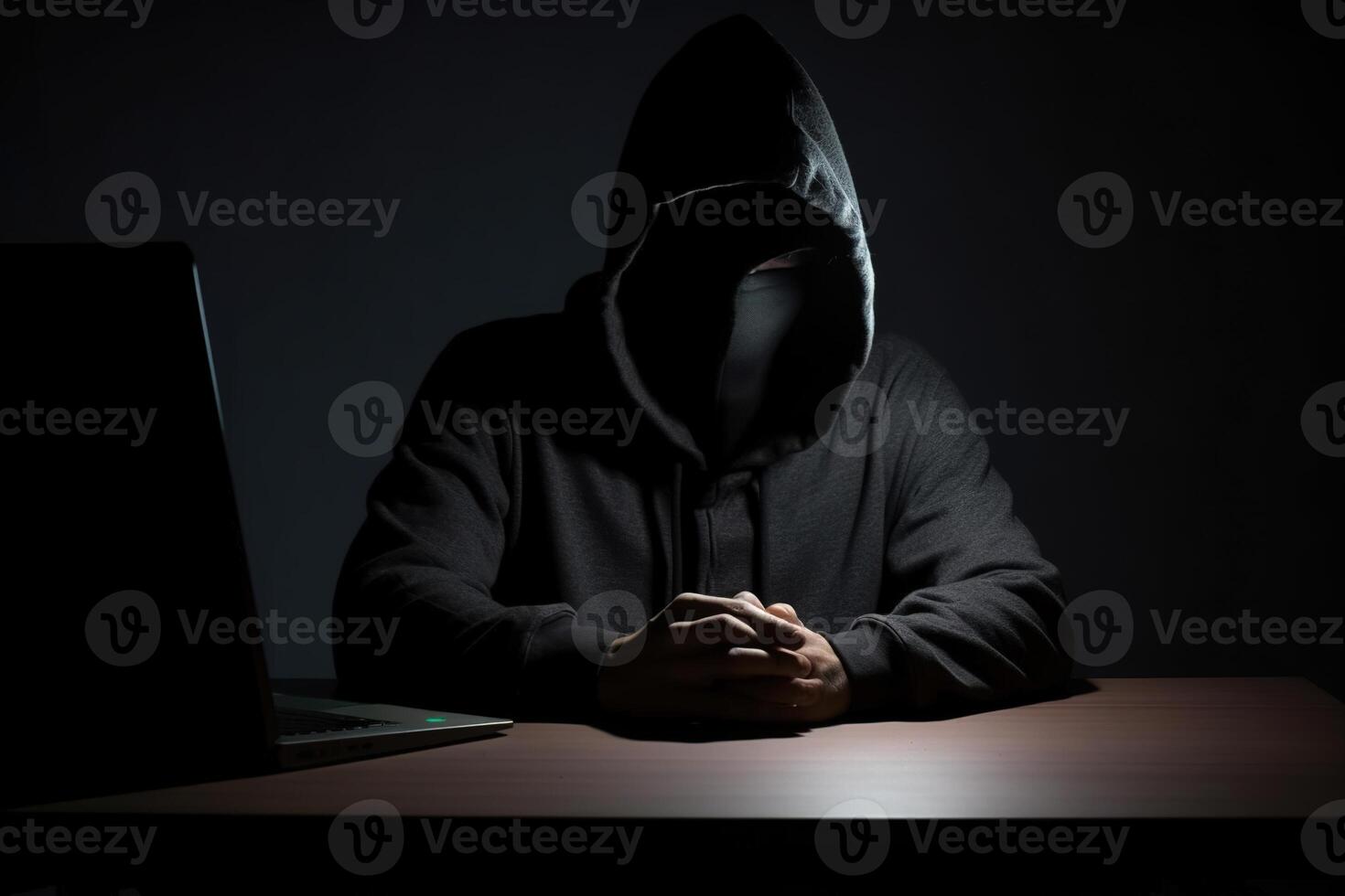 Hacker wearing black hoodie using laptop computer while working on dark background. photo