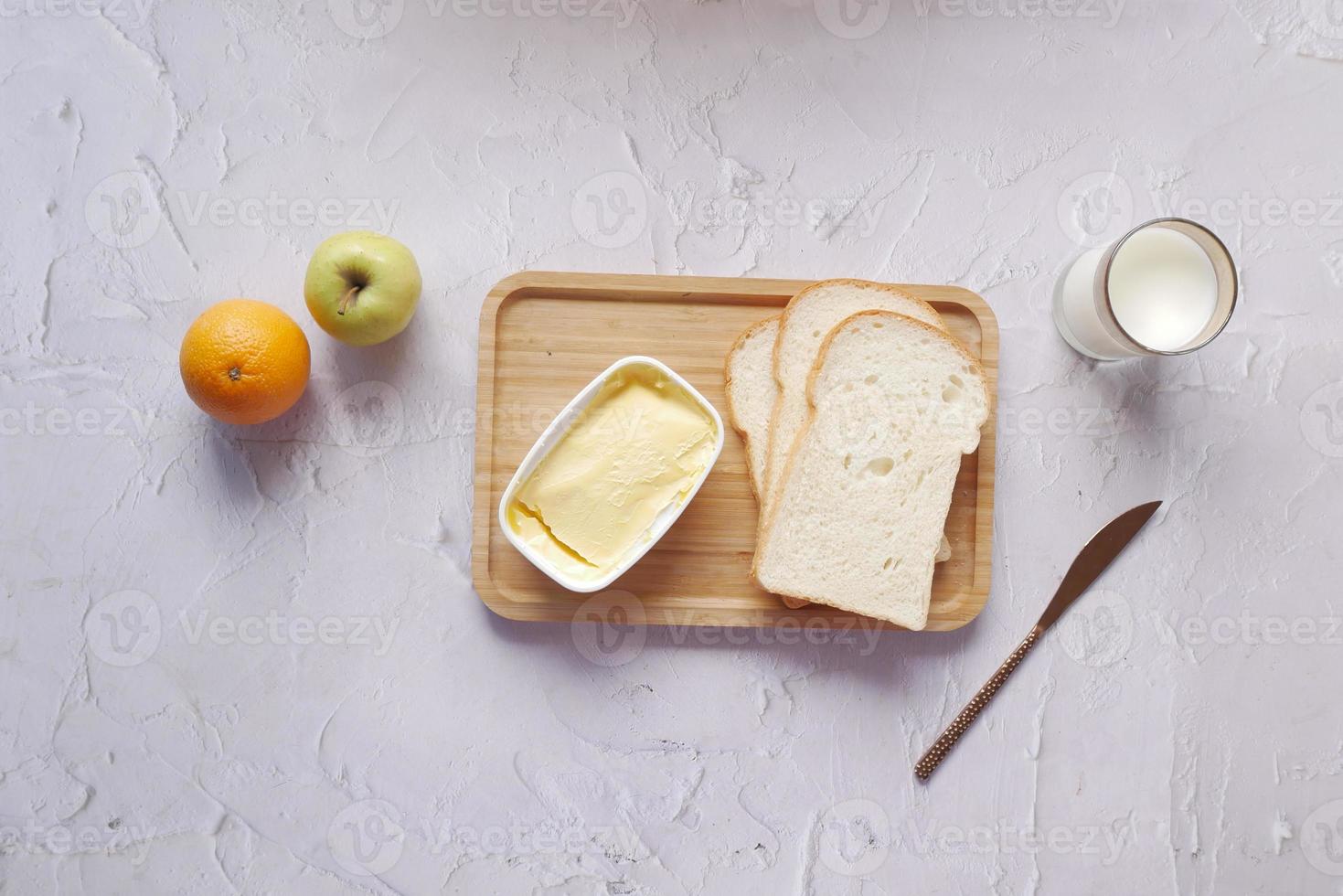 fresh butter in a container with bread , milk and apple on table photo