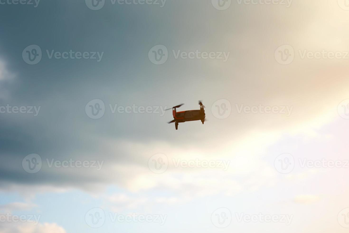 Hovering drone flying upward on a cloudy sky backdrop. copter flying . photo