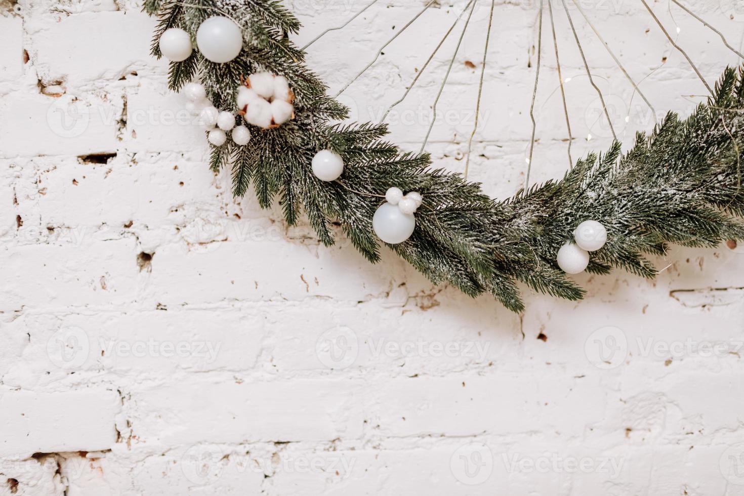 Christmas, New Year composition. Festive wreath with white balls made of Xmas tree, fir branches on white brick wall. Scandinavian cozy home decor. Happy Holidays, Template. Greeting card. 2023 photo