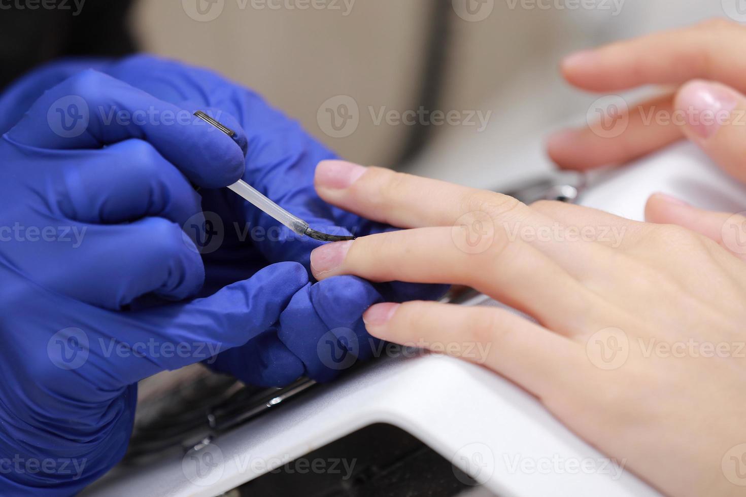Closeup shot of manicure in a beauty salon. Master during a manicure. Master manicurist varnishes the gel on the nails of a female client. The concept of beauty and health. photo